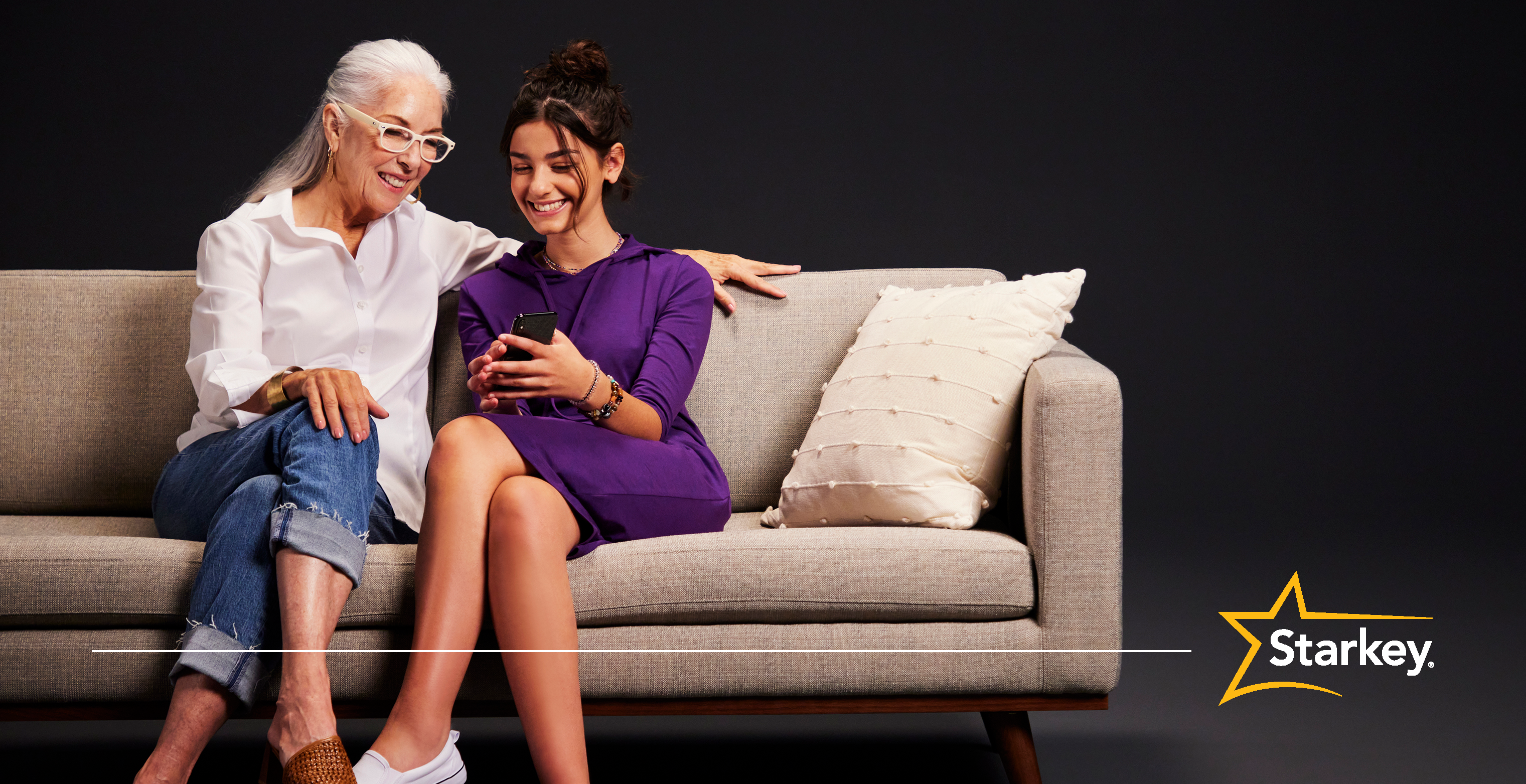 Senior woman sitting on a couch with her arm around young woman looking at a phone